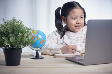 Asian kid girl writing follows teacher for learning an online lesson by video call the Internet...