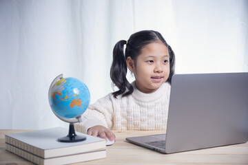 Asian kid girl writing follows teacher for learning an online lesson by video call the Internet...