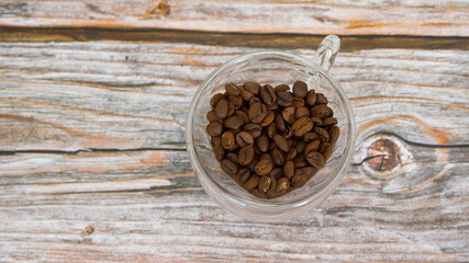 Heart shaped glass cup with coffee beans on wooden background