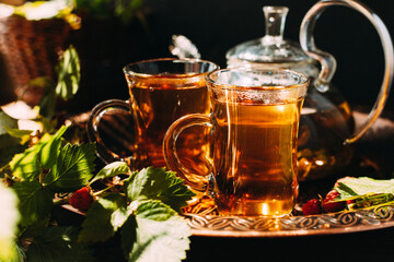 tea is poured into glass mugs. A teapot and a cup of tea stand on a copper tray next to raspberry leaves and berries