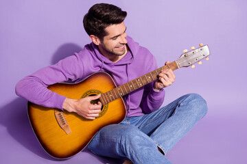Portrait of attractive cheerful guy sitting playing guitar hit song isolated over purple violet...