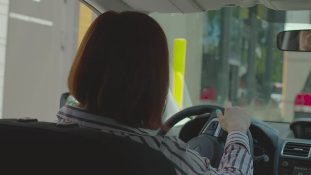 30s female driver paying bill with mobile phone and contactless terminal sitting in the car. Woman using NFC payment on her cellphone to pay for fast food restaurant. Taking away food from car.