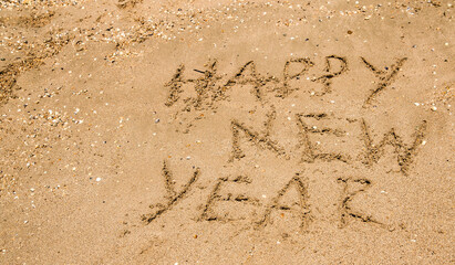 happy new year greetings are written on wet sea sand