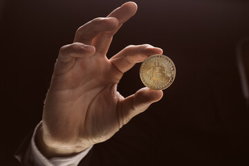 Plakat Close up man hand holding golden Bitcoin over black background
