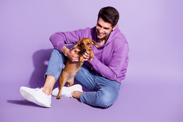 Portrait of attractive cheerful guy sitting spending free time with doggy puppy resting isolated...