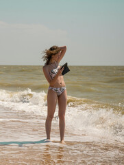 Naklejka premium a young slender girl stands on the seashore and poses for a photo with her phone