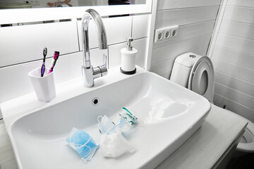Used medical masks lie in the sink waiting a washing. White color bathroom. Disinfecting and saving money to be used again. Reusable. Family health care and save the budget concept. Epidemic hygiene