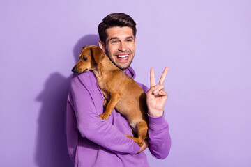 Photo portrait cheerful man smiling keeping little brown puppy showing v-sign isolated pastel...