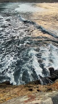 Destructive and impressive waves. Sea storm. Waves crash against coastal rocks, creating explosion of water. Overhead view of giant ocean waves crashing and foaming on beach with rocks. Vertical video