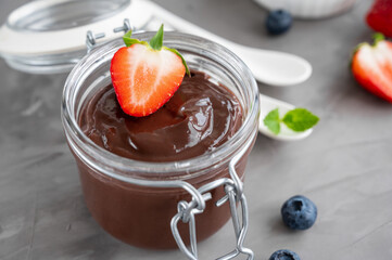 Chocolate pudding with fresh berries and whipped cream in a glass jar on a gray concrete...