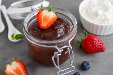 Chocolate pudding with fresh berries and whipped cream in a glass jar on a gray concrete background. Copy space.