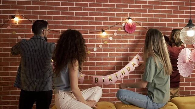 Friends preparing party indoors hanging garlands and hbirthday letters