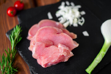 Chunks of sliced raw turkey meat, chopped onions, on a black slate background.