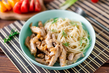 Fried meat and spaghetti on a plate on a wooden background with tomatoes and herbs.