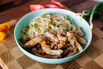 Fried meat and spaghetti on a plate on a wooden background with tomatoes and herbs.