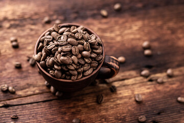 Coffee beans in a clay cup on a brown wooden old background.