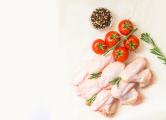 Fototapeta na wymiar Raw fresh chicken wings with aromatic rosemary and tomatoes. Top view of a serving of fresh chicken