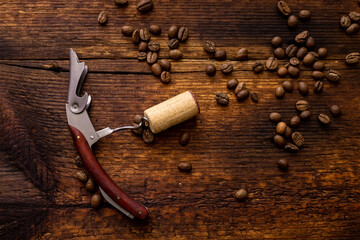 Corkscrew with a cork on a wooden background with coffee beans.