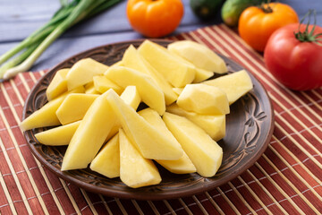 Tubers of raw peeled cut potatoes on a plate on the kitchen table with vegetables. Preparation for cooking.