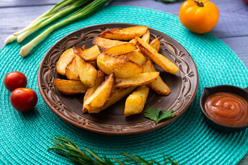 Fried potatoes in large pieces on a plate on a turquoise napkin on the table with different vegetables.