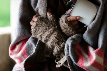 Hands wearing old gloves of homeless man holding jug for need money