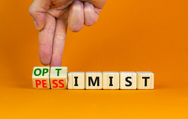 Pessimist or optimist symbol. Businessman turns cubes and changes the word 'pessimist' to 'optimist'. Beautiful orange table, orange background. Business, optimist or pessimist concept. Copy space.
