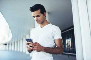 Young hipster guy in casual clothes connecting to wireless for chatting and messaging in social media networks, Caucasian man checking mobile sms writing text for sending via smartphone application