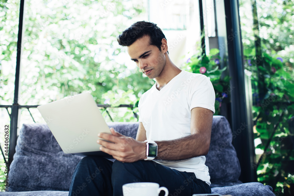 Poster caucaisan male freelancer in casual clothes browsing web information on modern laptop computer while