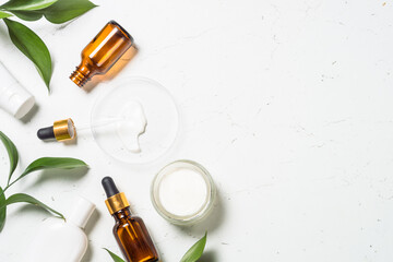 Natural Cosmetic laboratory. Cosmetic bottles, cream, serum, sea salt and green leaves at white table. Flat lay image.