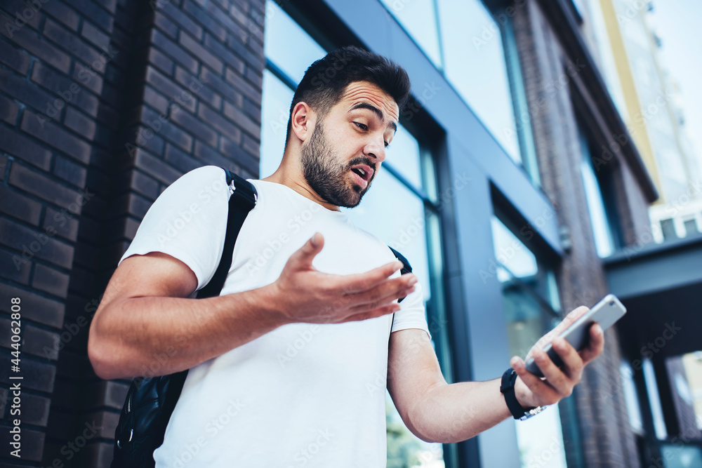 Poster shocked hipster guy checking received email message on smartphone device using 4g in roaming during 