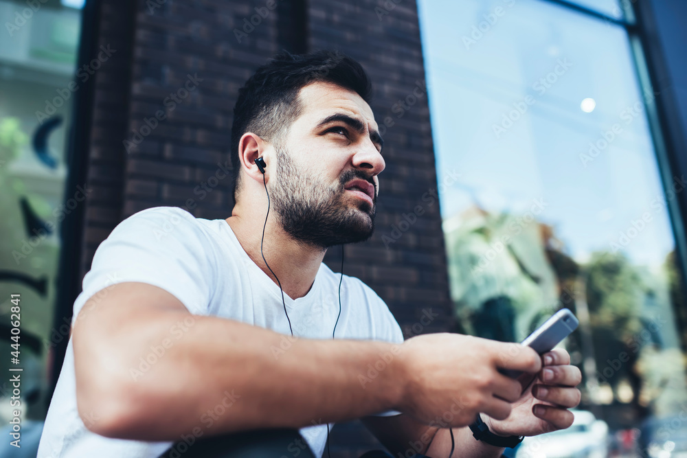 Aufkleber puzzled hipster guy with modern cellphone technology thinking about web networking while listening o