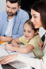 Fototapeta premium woman using laptop while assisting daughter in homework together with husband