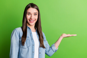 Portrait of attractive cheerful amazed girl holding on palm copy blank space gift present isolated over bright green color background