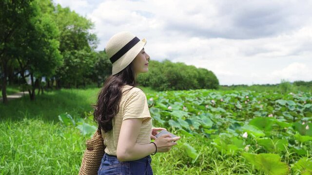 happy asian woman is appreciating the beauty of the lotus field in the wild after taking photos with a mobile phone on a sunny day at dapo pond taitung, taiwan