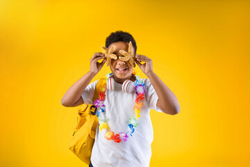 Happy boy holding sea stars wearing hawaiian lei flower necklace with backpack on yellow background