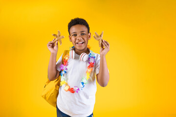 Happy boy holding sea stars wearing hawaiian lei flower necklace with backpack on yellow background