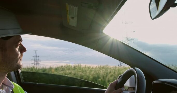 Young man in helmet drives modern car past lush green field with power transmission lines on spring day extreme close view