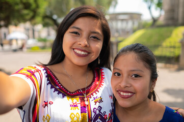 Two sisters or friends taking a selfie with the phone in the park of Quetzaltenango, Guatemala,...