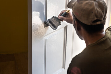 Person painting wooden white door with paint brush during home rennovation. Motion blur intended.