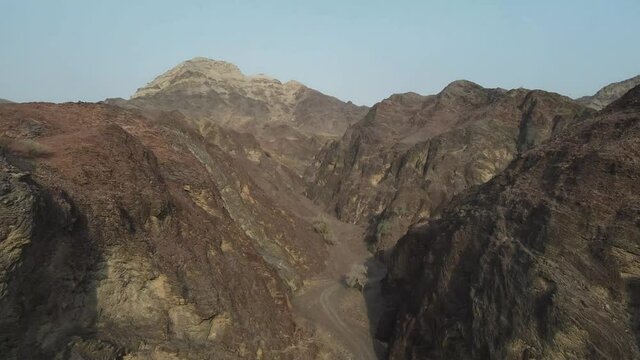 An aerial slow cinematic 4k video over the Hajar Mountains in the UAE showing red and brown rugged mountains 