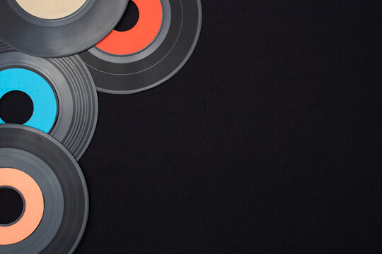 Multi colored 7 inch single vinyl records on a black background placed on top left corner with empty space for text. Top down view flat lay. Retro or music concept