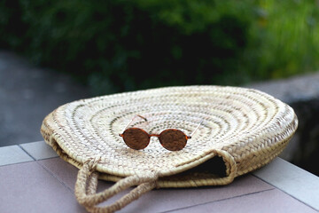 Round straw bag and retro sunglasses in a garden. Selective focus.