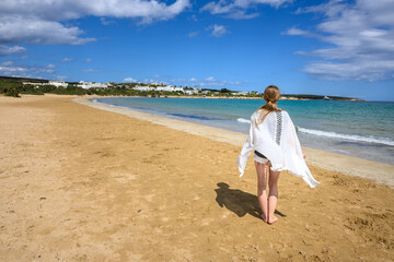 A young woman stands on the seafront. Santa Maria beach on Paros island. Cyclades, Greece