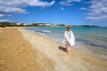 A young woman stands on the seafront. Santa Maria beach on Paros island. Cyclades, Greece