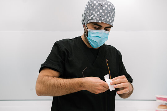 Male doctor in medical mask cleaning eyeglasses