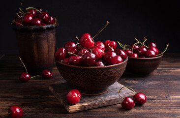 Ripe cherries in clay bowls on a dark wooden table, useful summer berries.