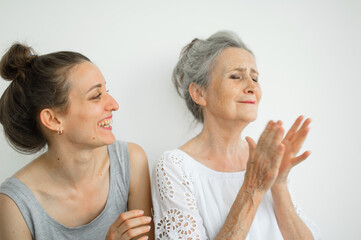 Happy senior mother is hugging her adult daughter, the women are laughing together, sincere family of different age generations having fun on white background