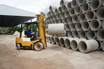 A yellow forklift truck is lifting reinforced concrete drainage pipe. Industrial building...