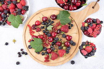 Wooden cutting board with summer berries raspberries, strawberries, currants, sweet cherries on a white background.