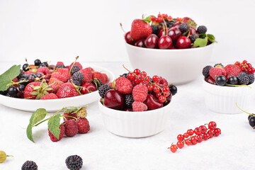 Plates with various berries on a white background, summer harvest.